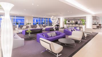 A modern hotel lobby with purple sofas, white chairs, and a central bar area.