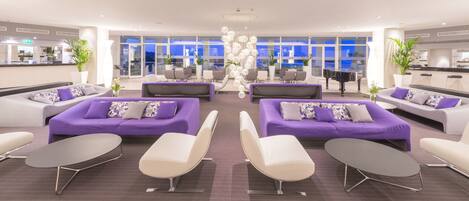 Eine moderne Lobby mit violetten Sofas, weißen Sesseln und einem Klavier.