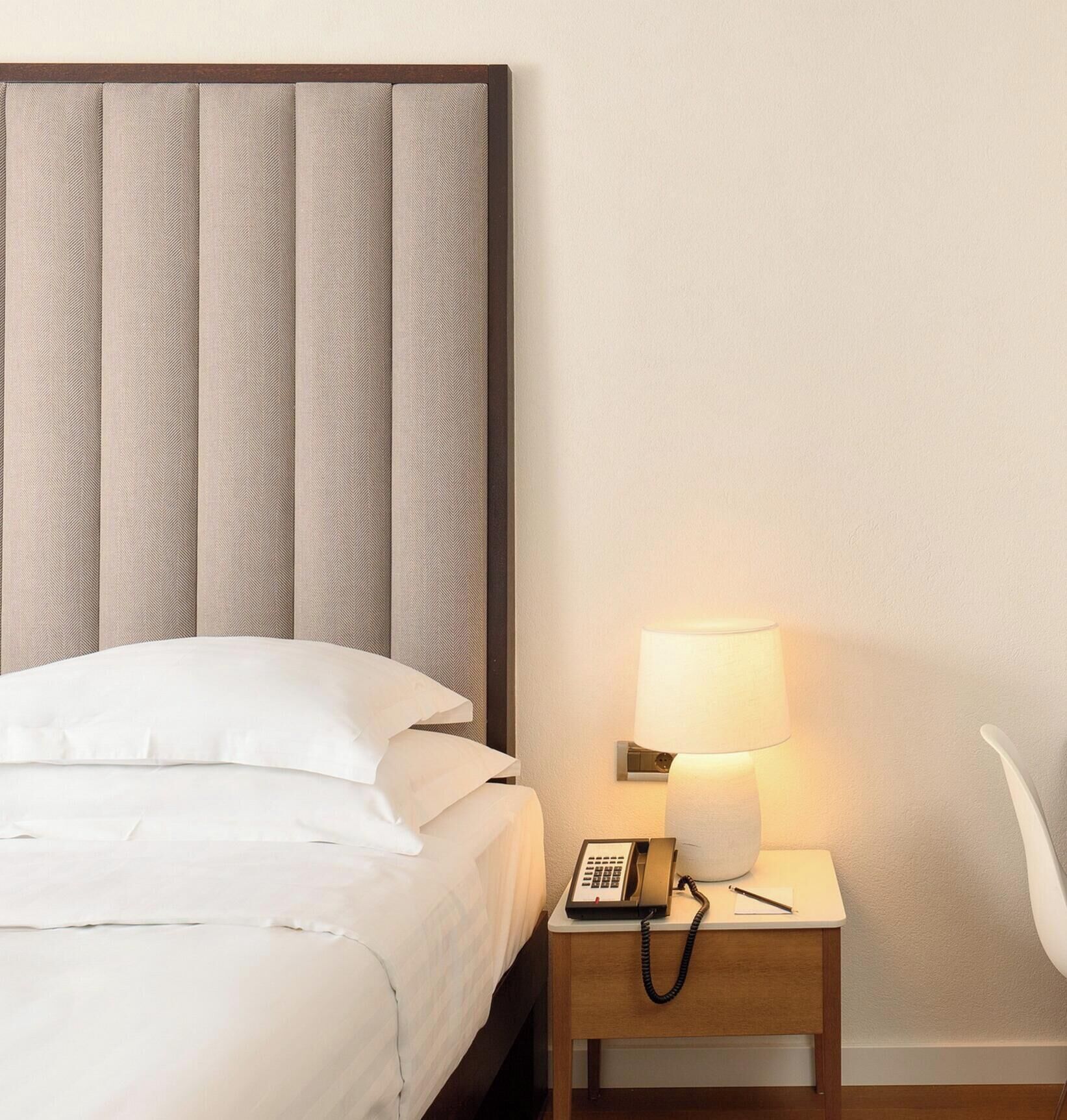 A hotel room with a bed, a nightstand with a lamp, and a telephone.