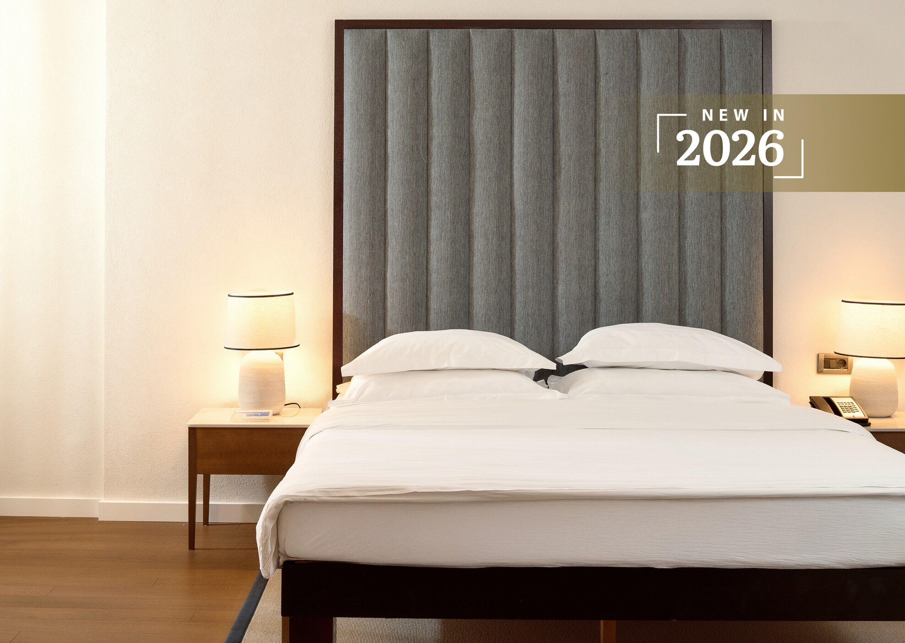 A hotel room with a large bed, two bedside tables with lamps, and a headboard with curtains.