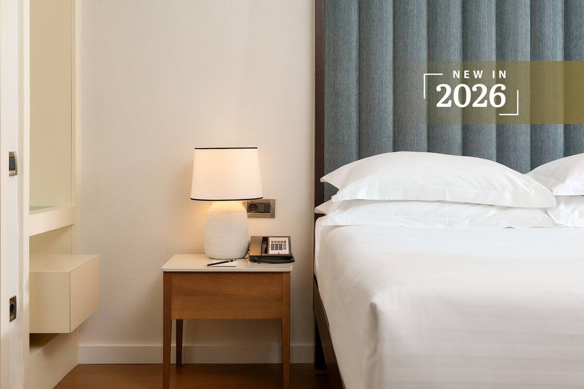 Ein Hotelzimmer mit einem Bett, einem Nachttisch mit Lampe, einem Telefon und einem an der Wand montierten Radio.