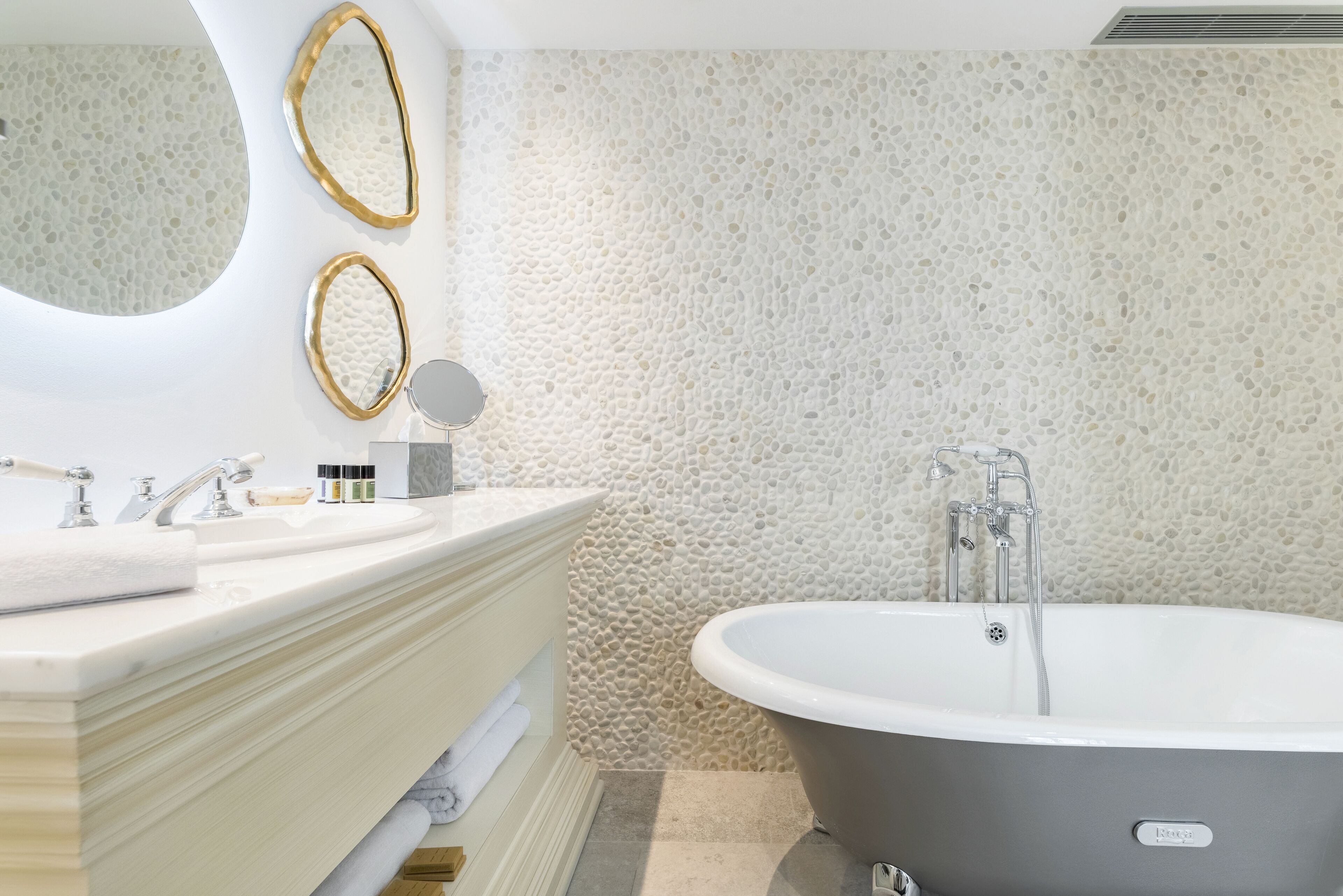 Ein modernes Badezimmer mit einer freistehenden Badewanne, einem Waschtisch mit Spiegel und einer Wand mit Struktur.