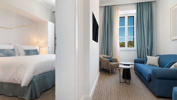 Habitación de hotel con cama, sofá, sillón, una mesita y ventana con cortinas.