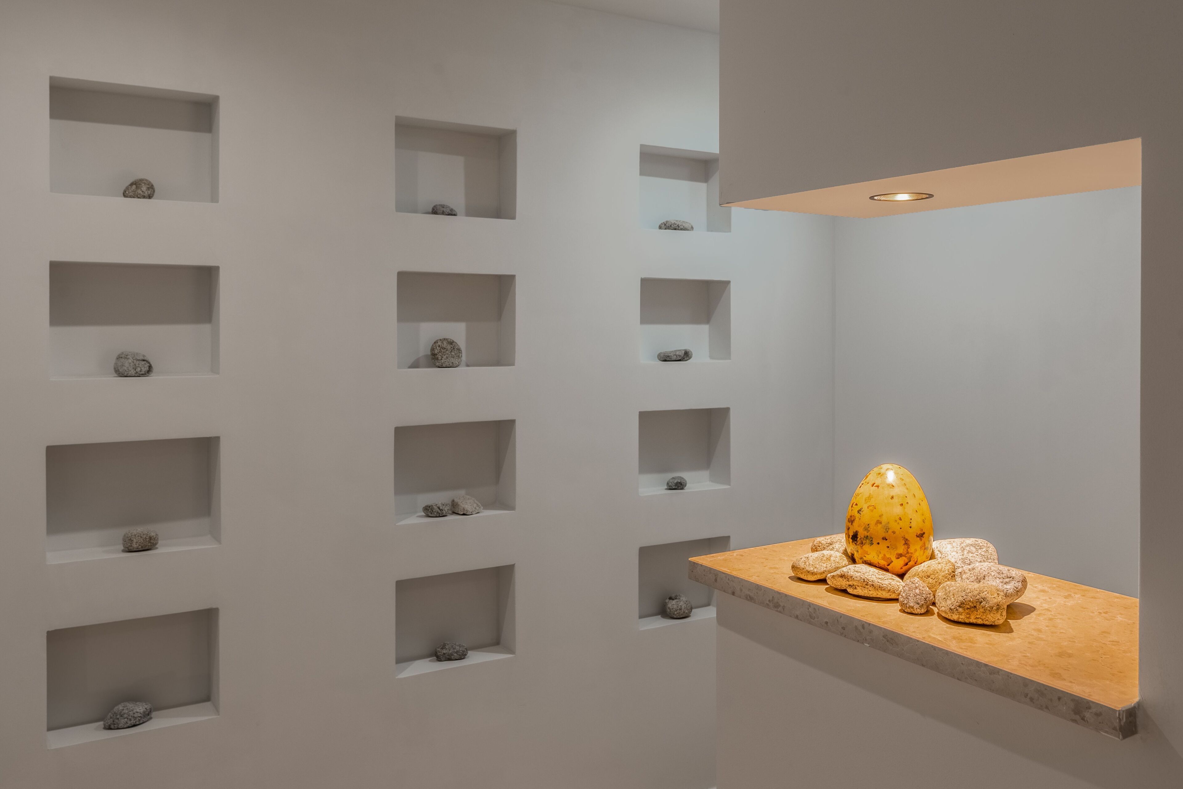 A modern interior with multiple white shelves displaying rocks and a wooden counter with decorative items.