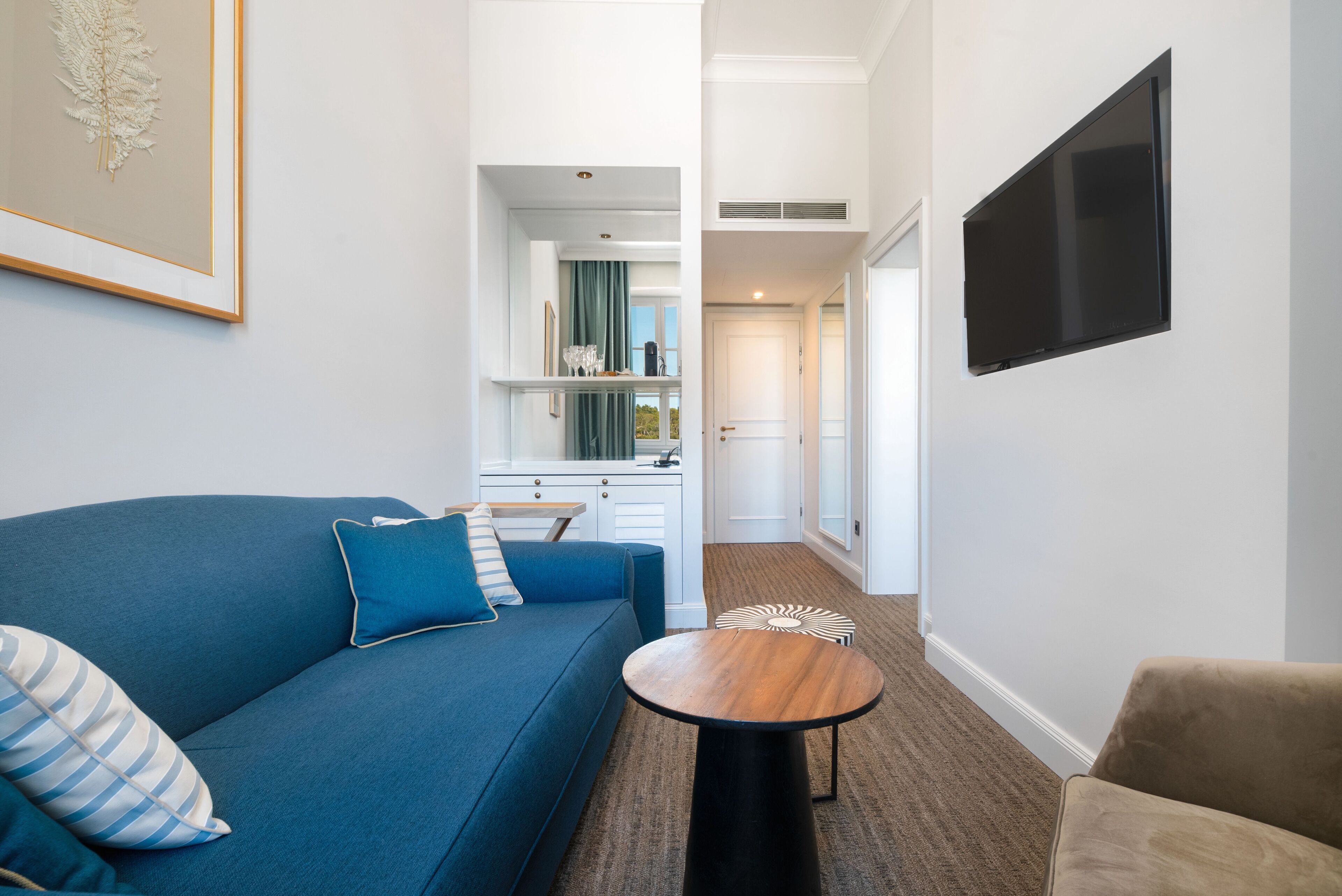 A modern living room with a blue sofa, a round coffee table, and a flat-screen TV mounted on the wall.