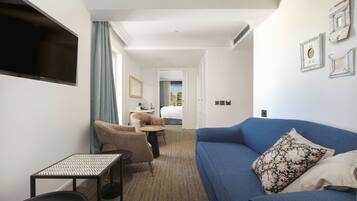 Habitación de hotel con un sofá azul, una mesita pequeña, una silla y un televisor montado en la pared.