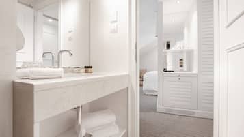 Een moderne badkamer met een marmeren wastafel, een grote spiegel en een inloopkast met witte deuren en planken.