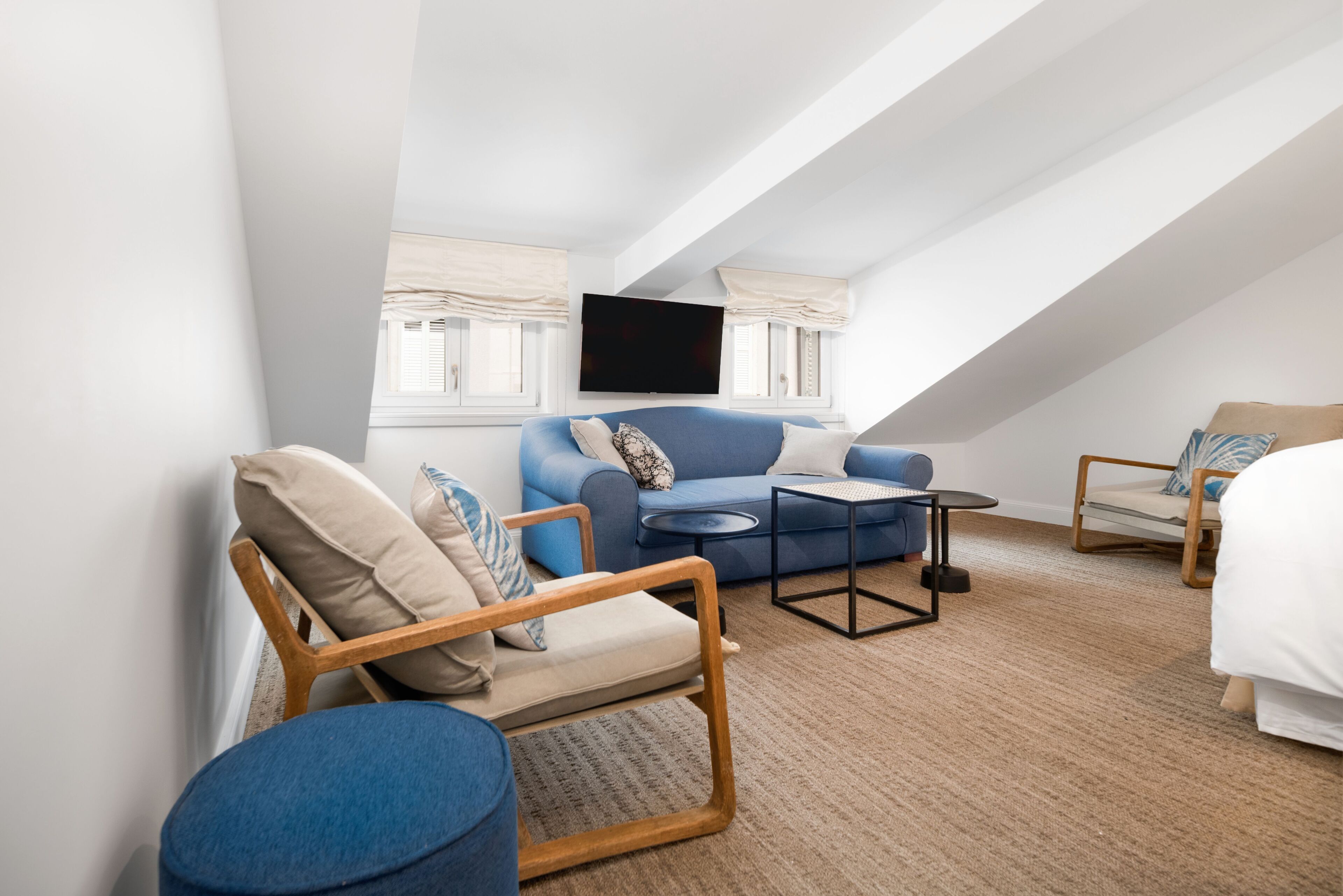 A modern, well-lit room with a blue sofa, a wooden chair, a small round table, and a bed.