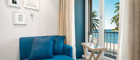 A room with a blue sofa, a small table with a bottle, and a view of the sea through a balcony.