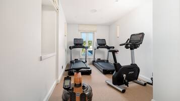 Een huisgym met loopbanden, een elliptische trainer en een hometrainer.