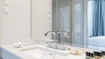 Un baño moderno con un espejo grande, un lavamanos y tocador. Hay artículos de aseo en la encimera y una toalla enrollada sobre ella.