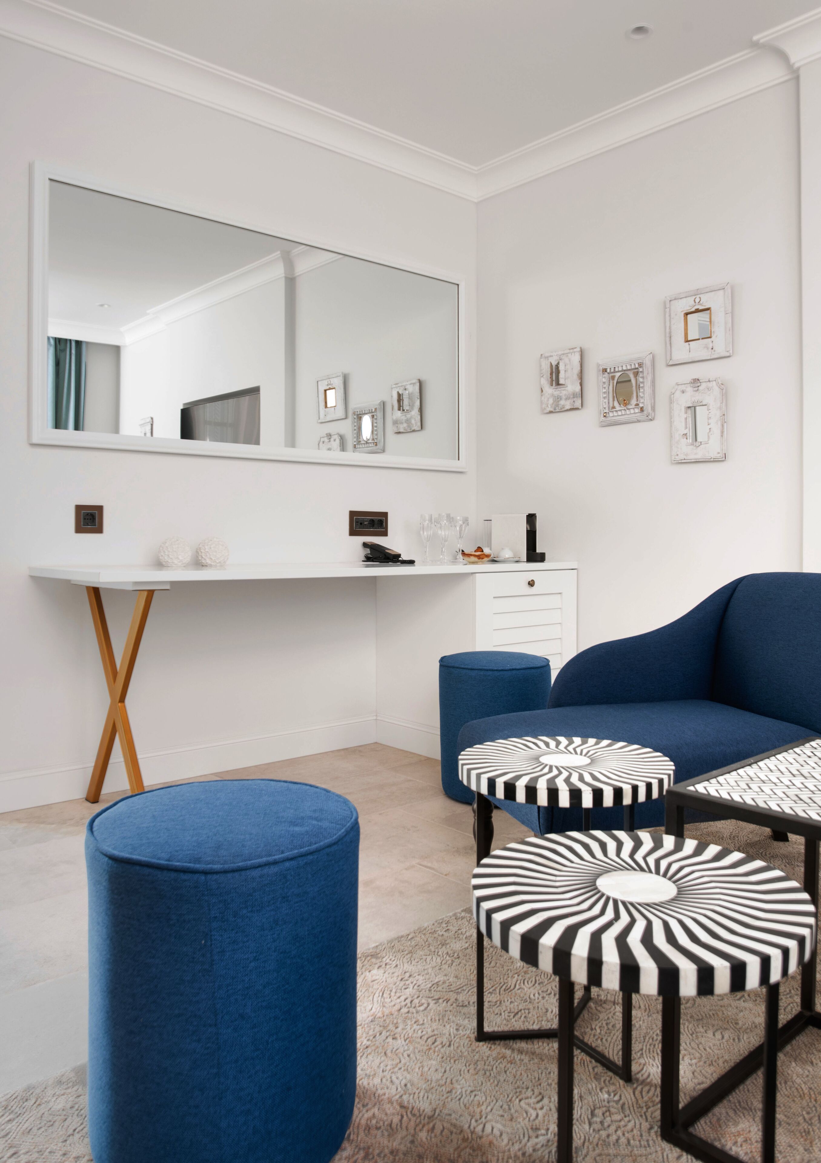 A modern bedroom with a large mirror, a blue sofa, two ottomans, and a white dresser.