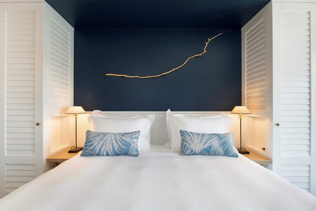Un dormitorio con techo oscuro, paredes blancas y una cama blanca con dos almohadas. Hay dos mesitas de noche con lámparas.