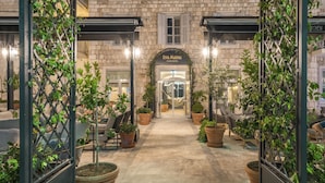 L’entrée de l’hôtel Riva Marina Hvar se distingue par sa façade en pierre, ses plantes en pot et un chemin dégagé menant à l’entrée.