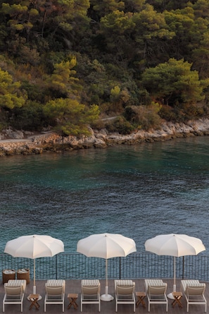 A poolside area with lounge chairs and umbrellas, overlooking a body of water and a wooded hillside. - Sirena Resort (Hvar)