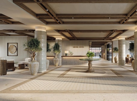 A spacious lobby with a reception desk, large columns, and potted plants.