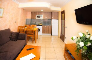 Un espacio habitable compacto con sofá, mesa de comedor y zona de cocina que incluye microondas, lavadora y refrigerador.