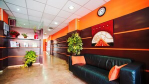En entréhall med en svart lädersoffa, krukväxter, en klocka på väggen och en receptionsdisk.