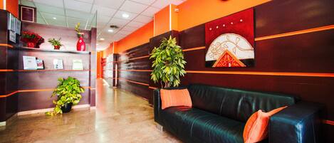 A lobby with a black leather couch, potted plants, a clock on the wall, and a reception desk.