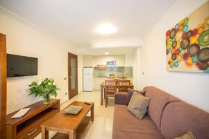Una sala de estar con sofá marrón, una mesa de centro de madera y un televisor en la pared.