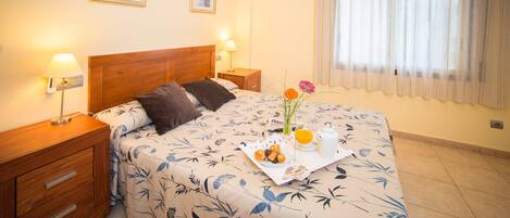 Een hotelkamer met een bed, twee nachtkastjes, een houten dressoir en een raam met gordijnen.