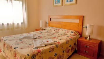 Una cama bien hecha con ropa de cama floral, un cabecero de madera, lámparas de noche y una mesita de noche con cajones.