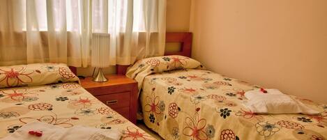 Una camera da letto con due letti, biancheria da letto floreale, un comodino e una finestra con tende leggere.