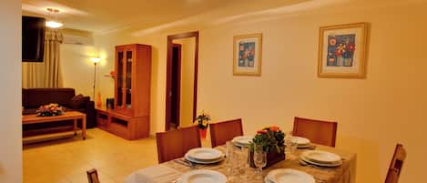 Un comedor con una mesa dispuesta para cuatro personas, rodeada de sillas de madera, en una habitación que también tiene un sofá y un aparador.