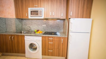 A compact kitchen with wooden cabinets, a built-in microwave, a sink, a dishwasher, and a refrigerator.