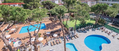 A rooftop pool area with multiple swimming pools, sun loungers, and umbrellas.