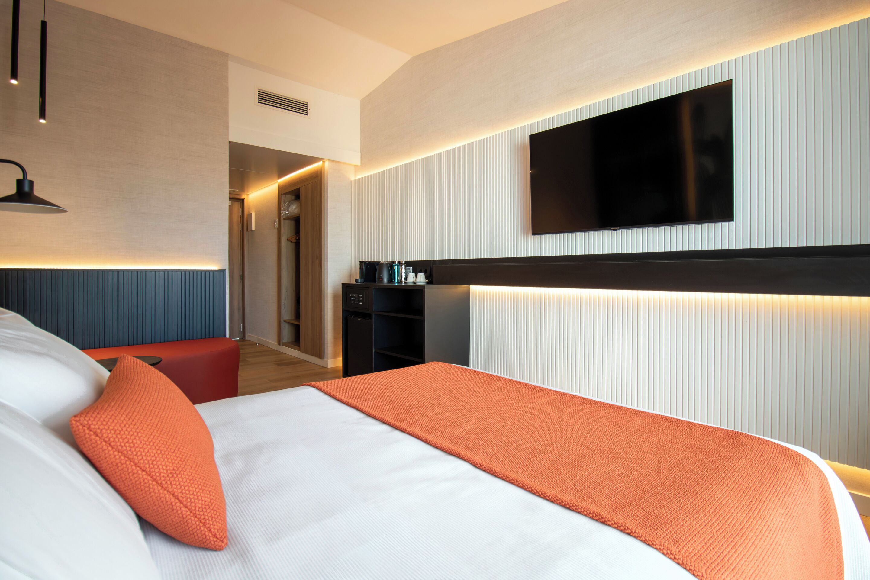 Une chambre d’hôtel moderne dotée d’un grand lit, d’un téléviseur à écran plat fixé au mur, d’un petit coin salon et d’une kitchenette.