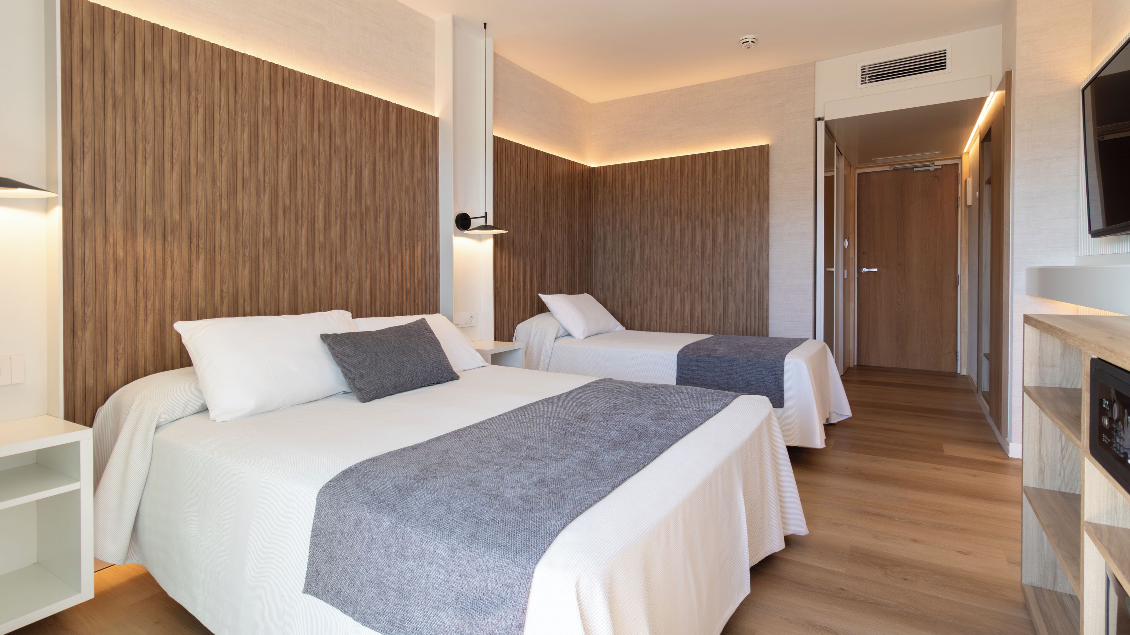 Habitación de hotel con dos camas, un televisor y una pared de madera.