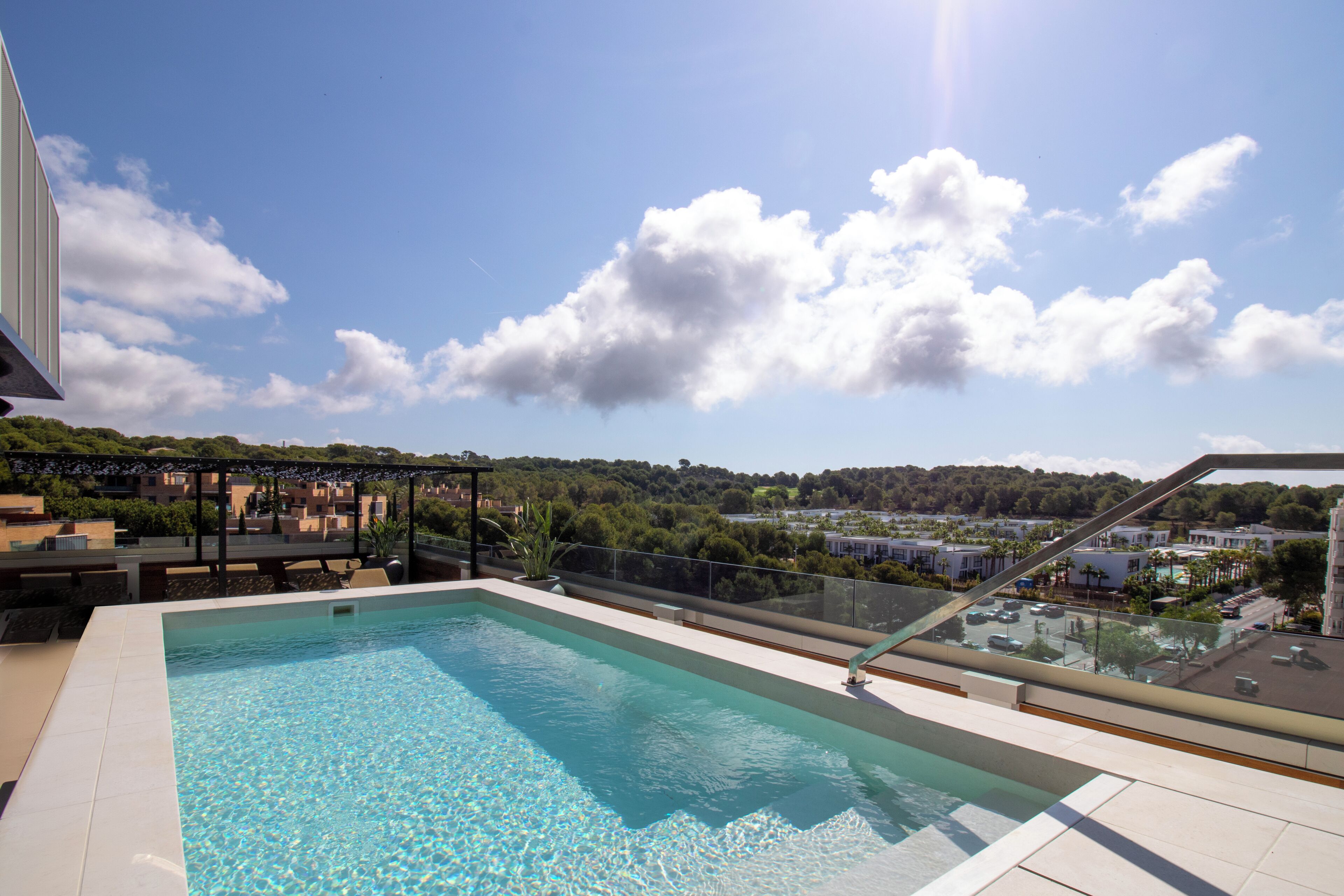 Une piscine sur le toit, avec une eau d’un bleu limpide, entourée d’une balustrade en verre, offrant une vue sur le paysage urbain et la verdure en arrière-plan.