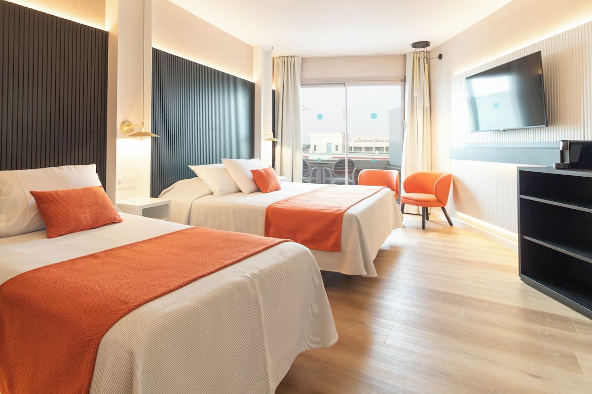 A hotel room with two beds, a TV, a desk, and a chair.