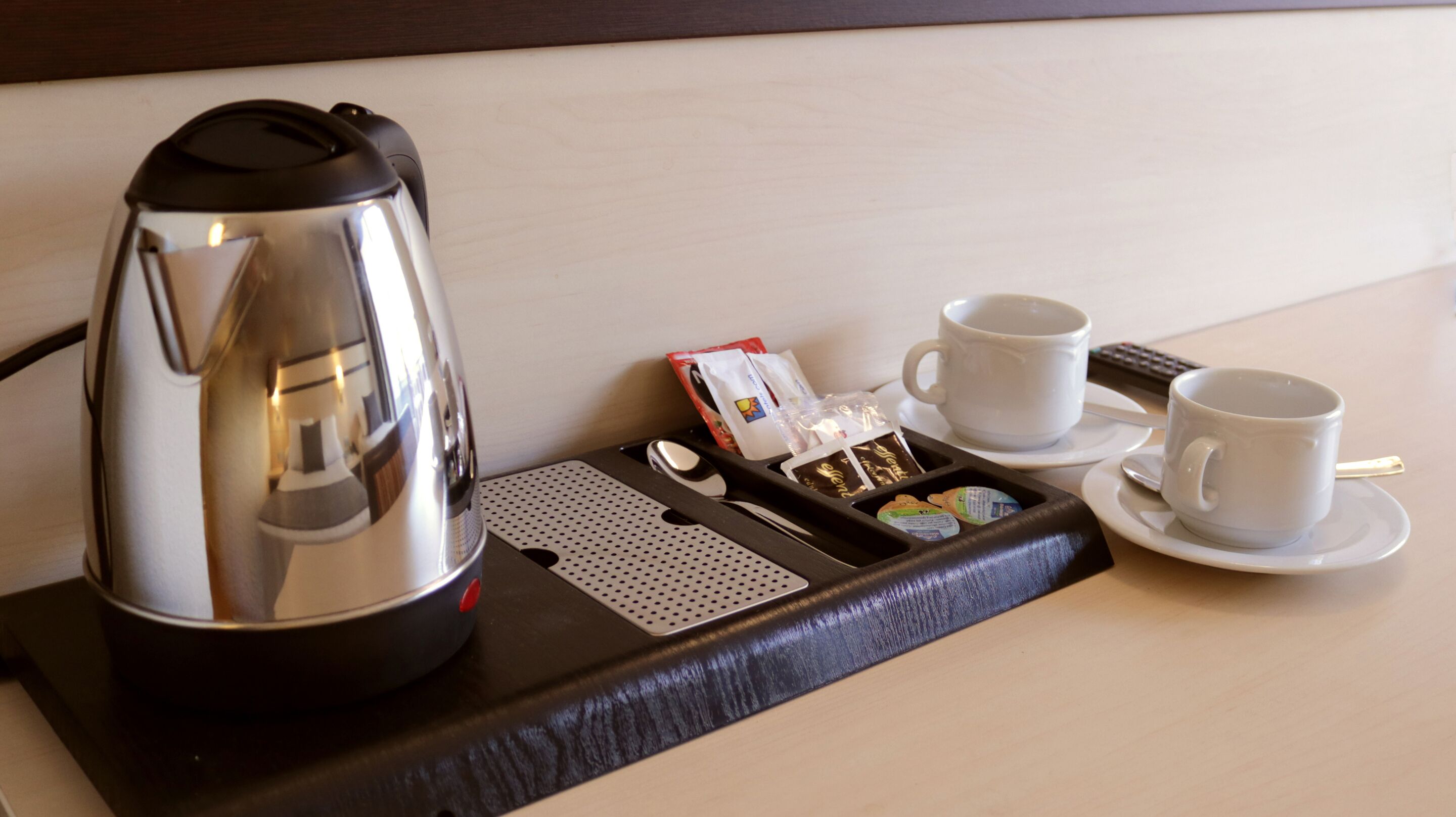 A hotel room's breakfast tray with a coffee maker, two cups, a spoon, a box of tea bags, and a packet of sugar.