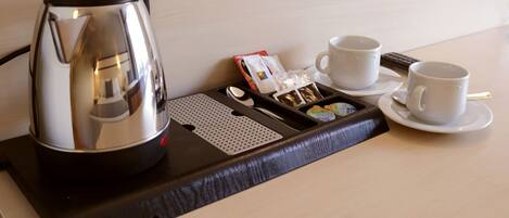 A hotel room's breakfast tray with a coffee maker, two cups, a spoon, a box of tea bags, and a packet of sugar.
