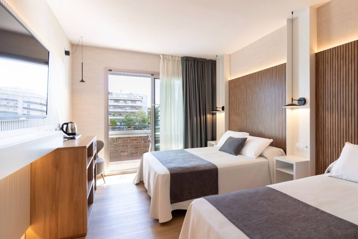 A hotel room with two beds, a desk, and a view of the city.