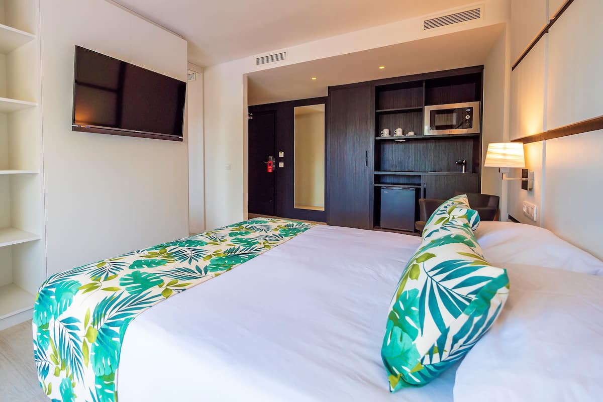 A hotel room with a bed, a TV mounted on the wall, a microwave, and a small seating area.