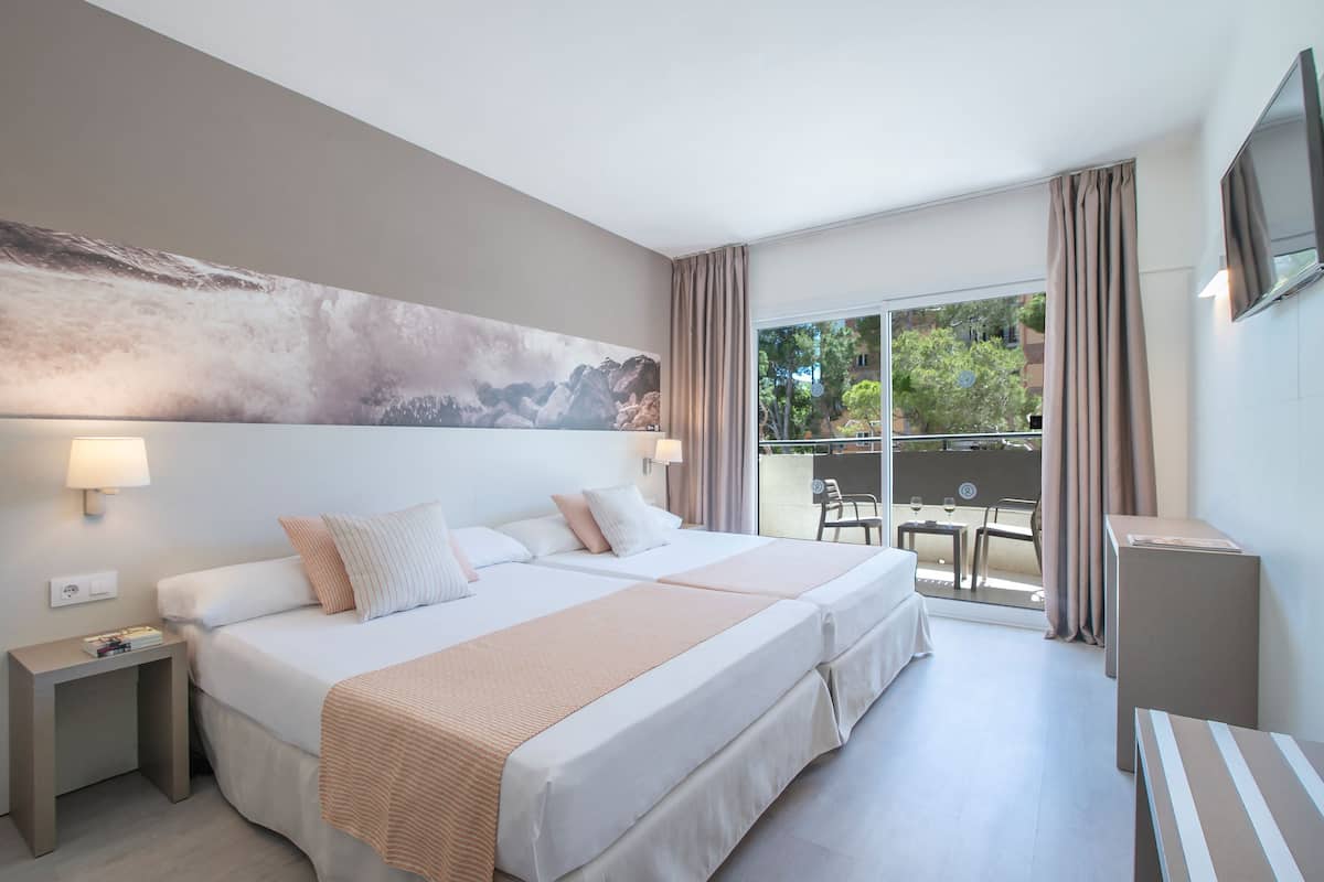 Een hotelkamer met twee bedden, een groot schilderij aan de muur, een balkon met een tafel en stoelen, en een aan de muur bevestigde televisie.