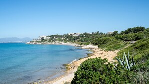 Un paysage côtier avec une plage, une eau d’un bleu limpide et des bâtiments situés sur une colline.