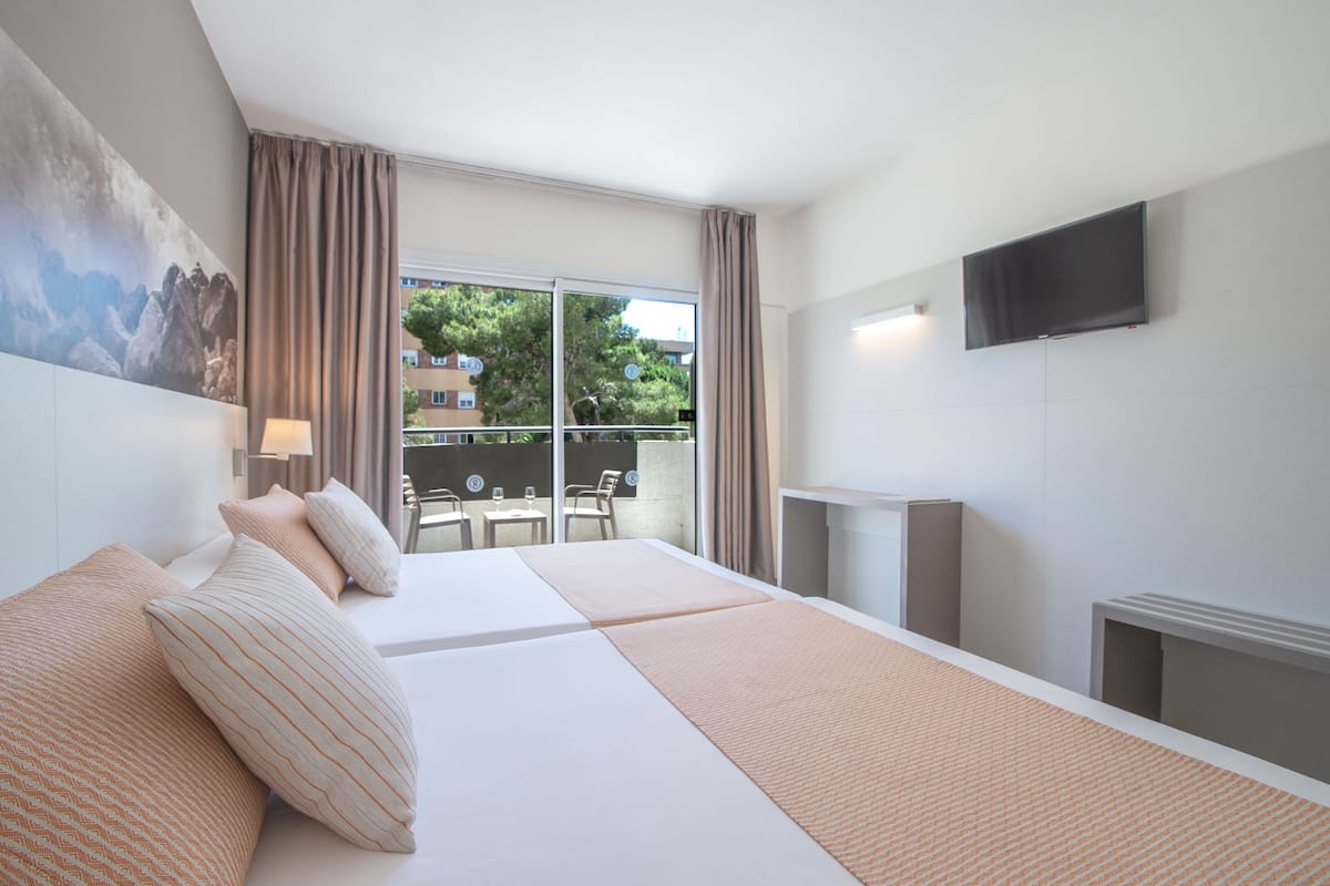 Een hotelkamer met een groot bed, een flatscreen televisie, een balkon met een tafel en stoelen, en een schilderij aan de muur.