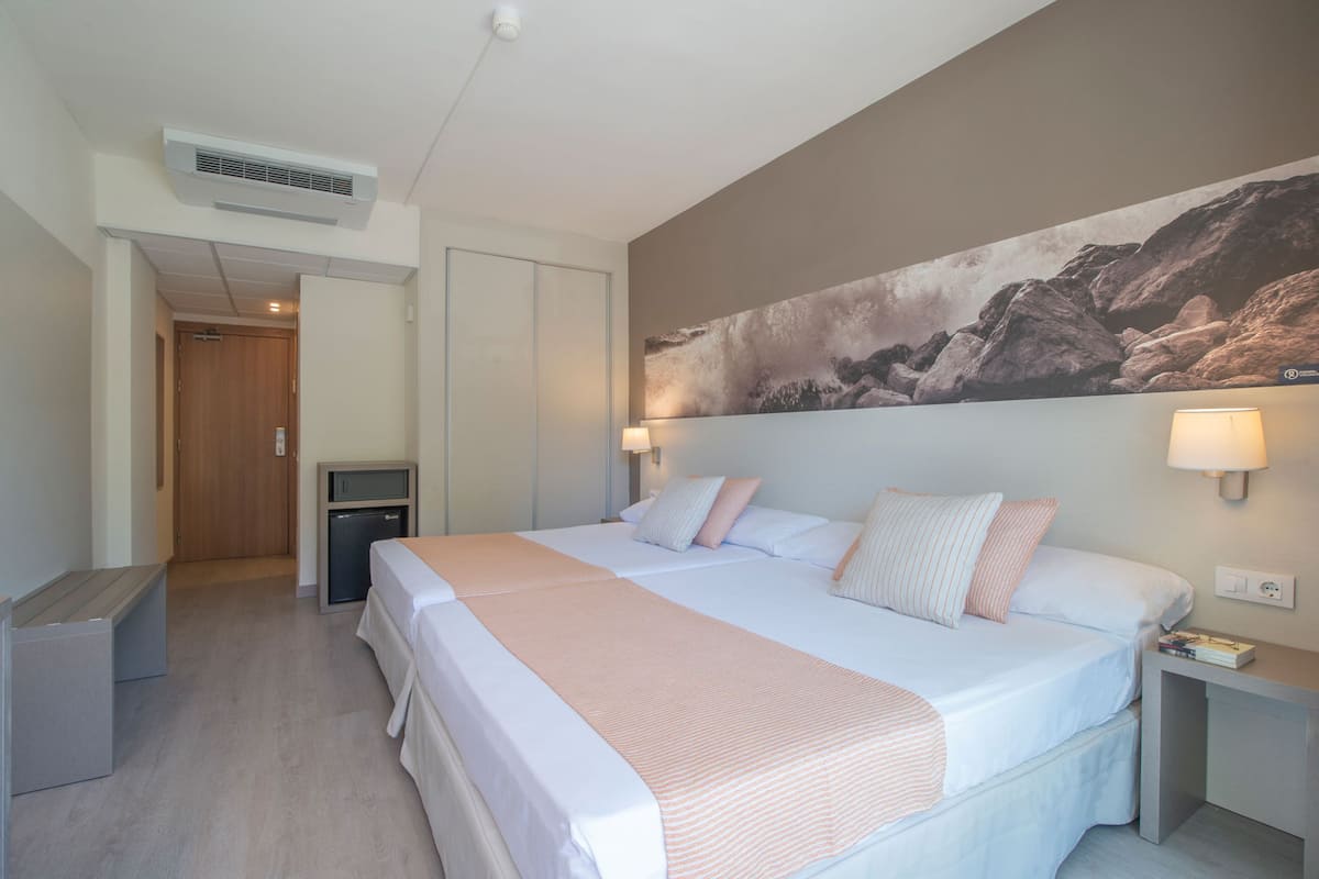 Een hotelkamer met een groot bed, nachtkastjes, een bureau, een kledingkast en een schilderij aan de muur.