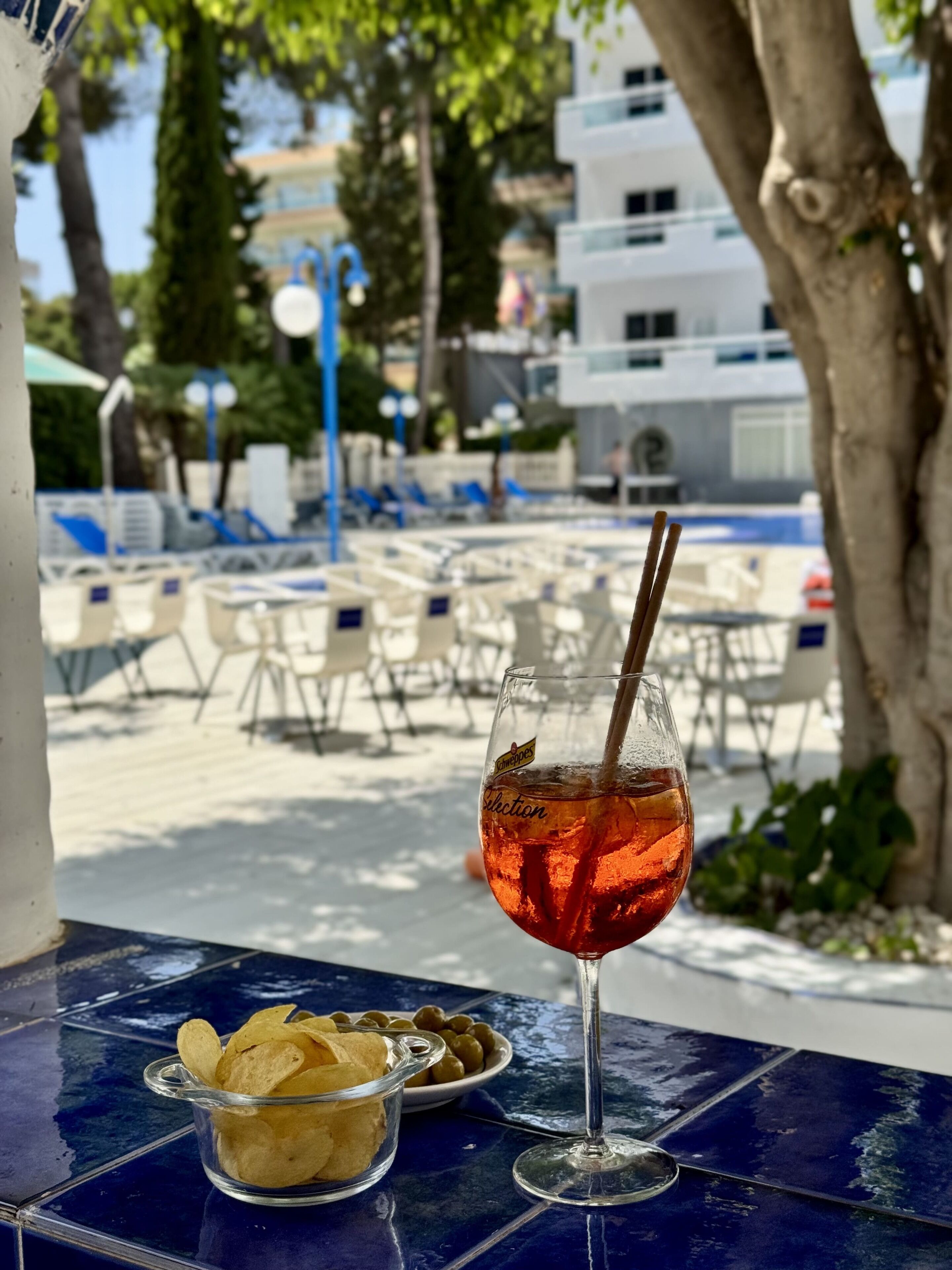 A glass of iced tea with a straw on a blue table, a bowl of chips, and a small bowl of olives.