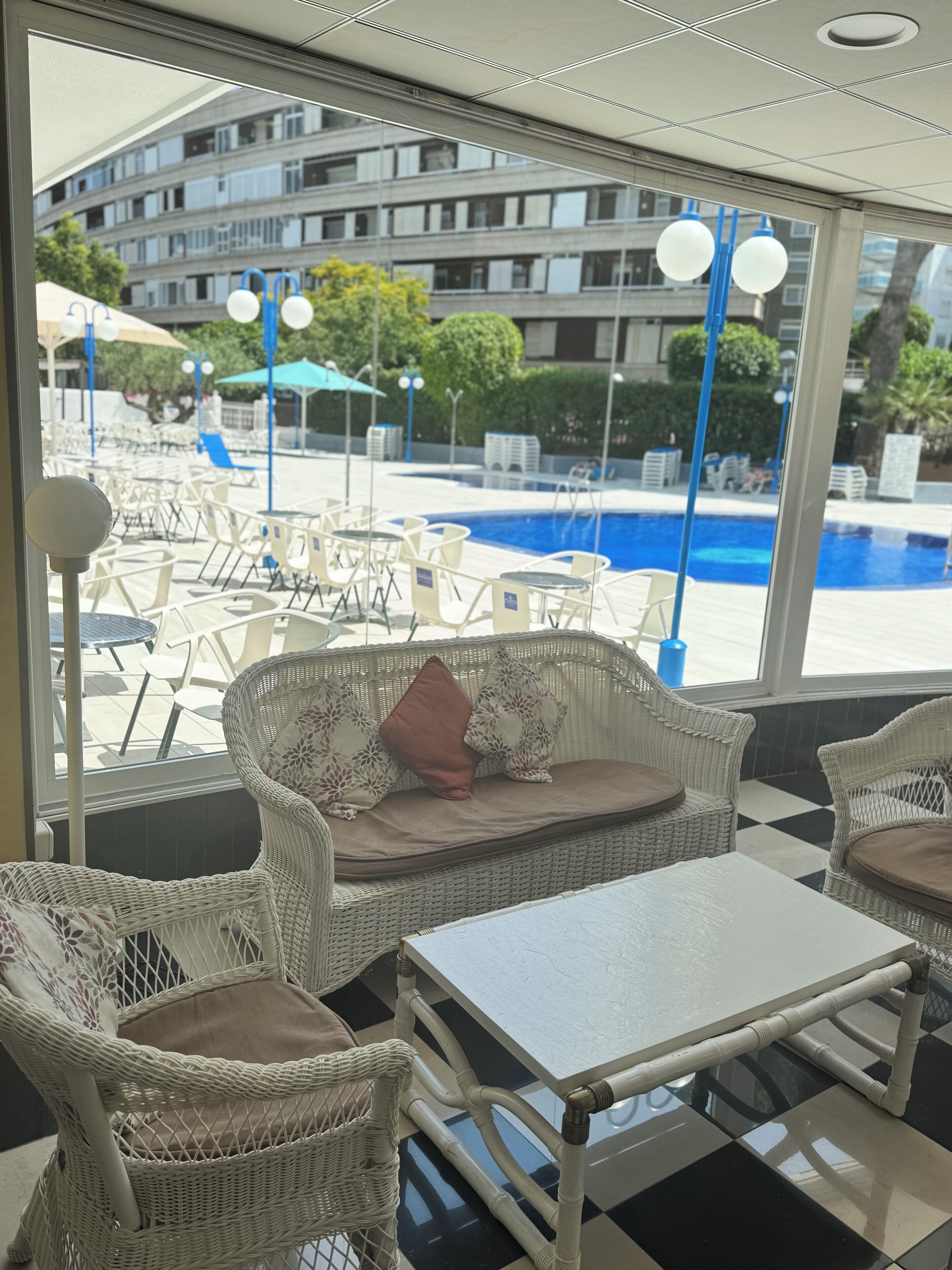 Zona de descanso junto a la piscina con mobiliario de mimbre y vistas a una alberca.