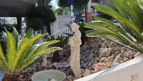 Un jardín con una estatua, palmeras y una fuente.