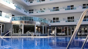 Een hotel met meerdere verdiepingen en een centraal gelegen zwembad, inclusief een gebogen glazen constructie en diverse balkons.