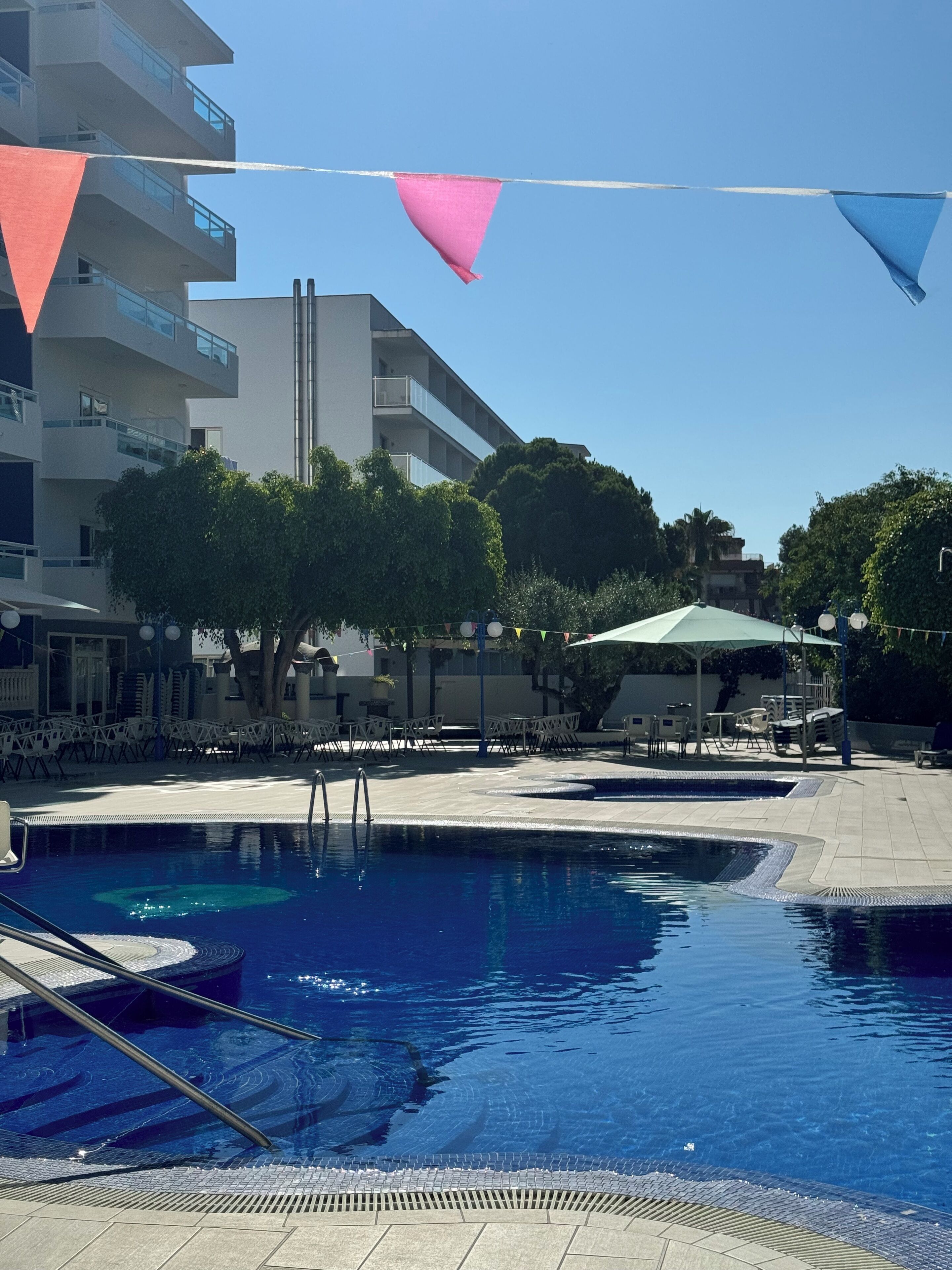 A swimming pool with a clear blue water surface, surrounded by lounge chairs and umbrellas, with a modern building in the background.