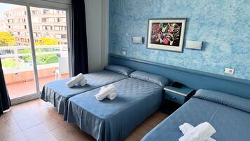 A hotel room with two beds, a window with a view of buildings, a framed picture on the wall, and a nightstand with a lamp.