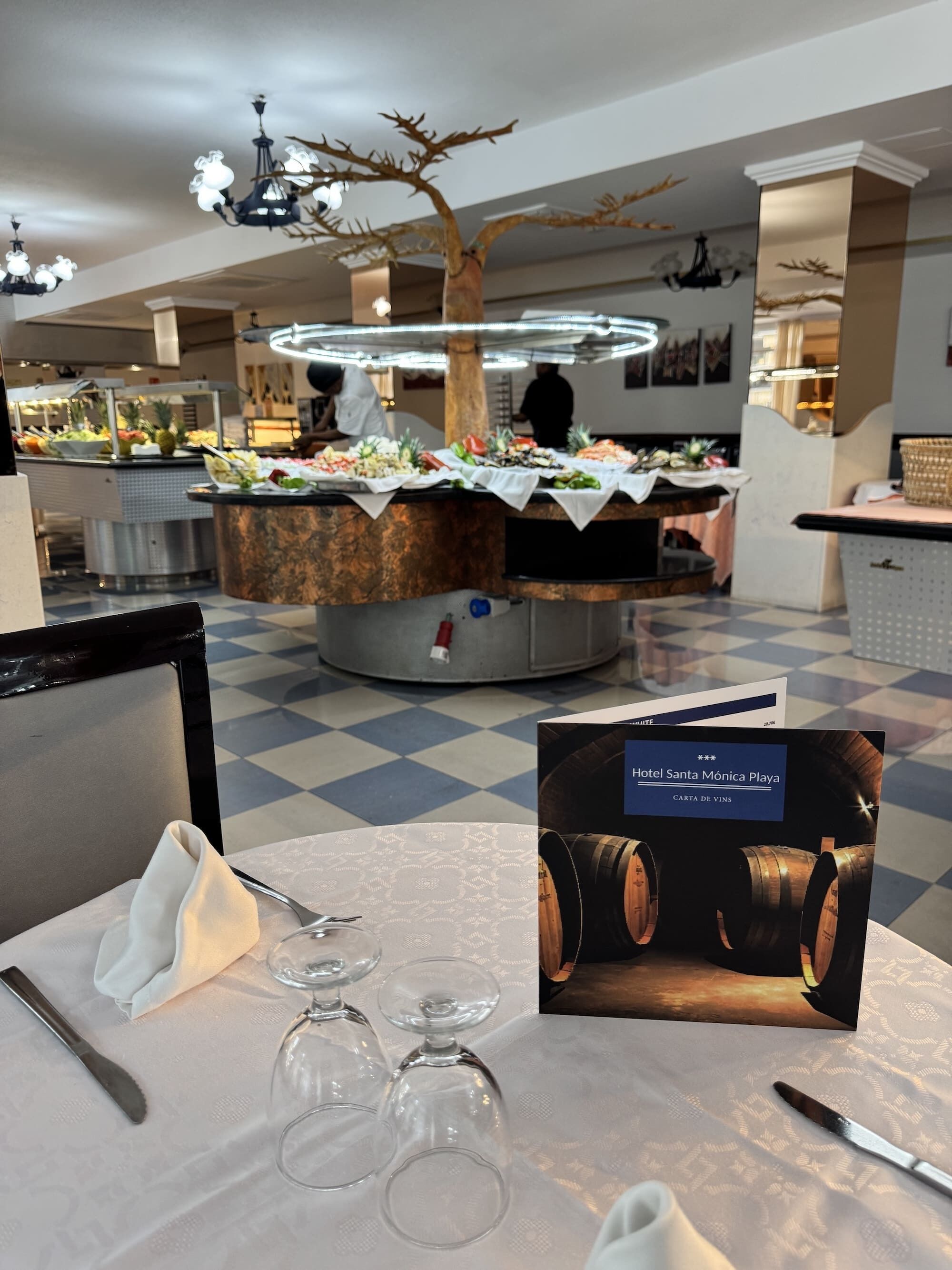 Un comedor con una mesa de buffet, copas de vino y un atril para el menú.