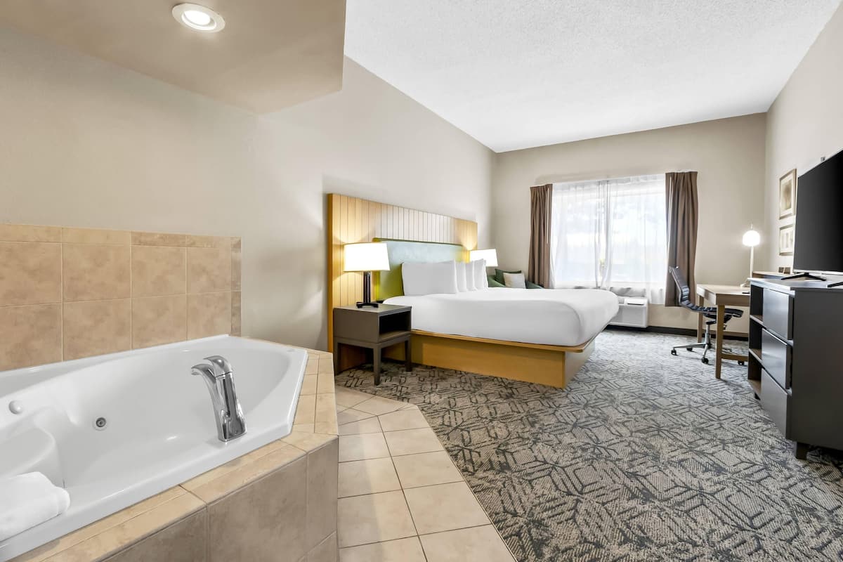 A hotel room with a large bathtub, two beds, a desk, and a television.